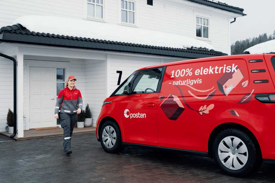 En postbud fra Posten leverer en pakke på døren til en bolig. Pakken inneholder en gave fra Gaveverket, klar til å overraske mottakeren.